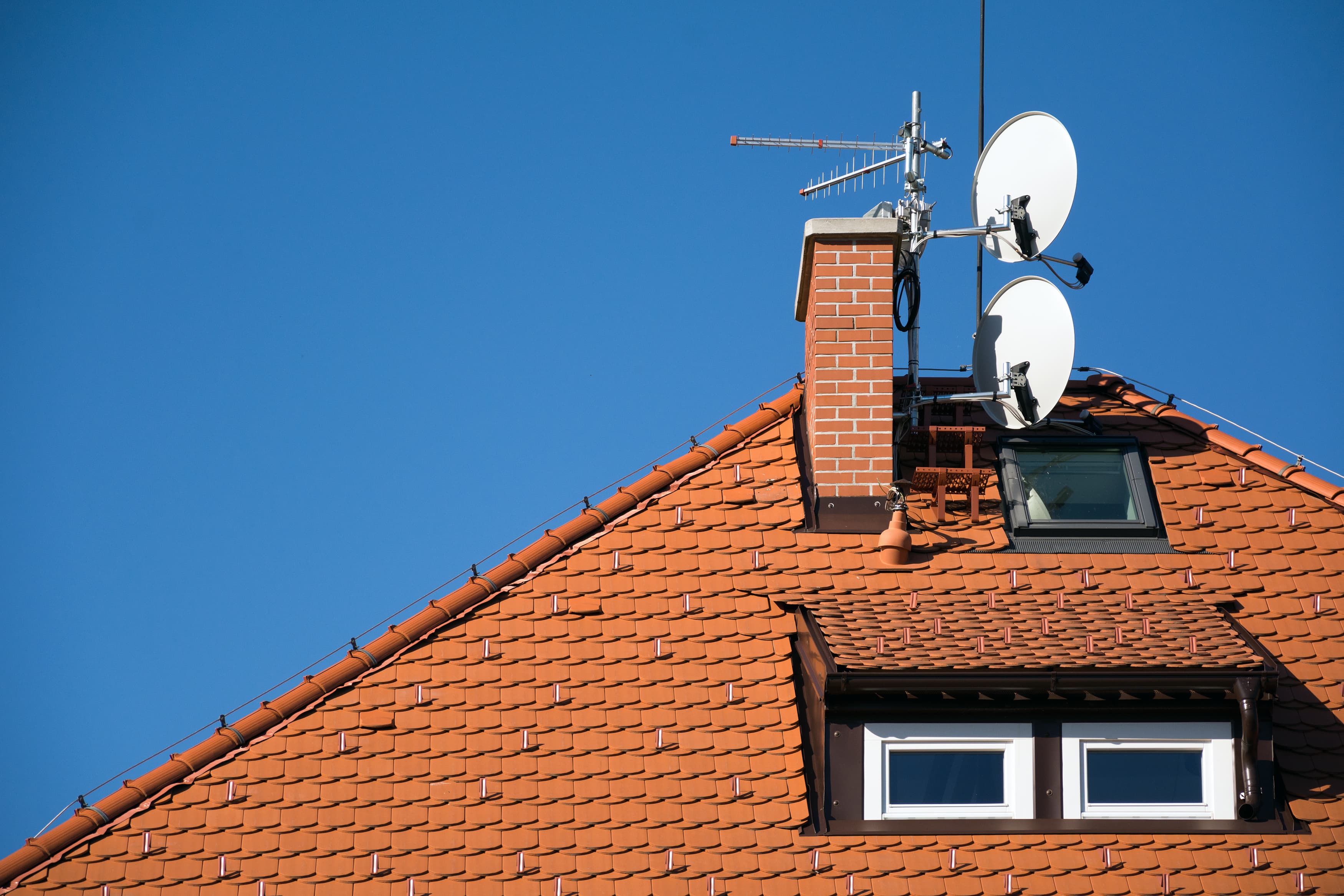 Satellite dishes mounted above a tiled roof under a clear sky
